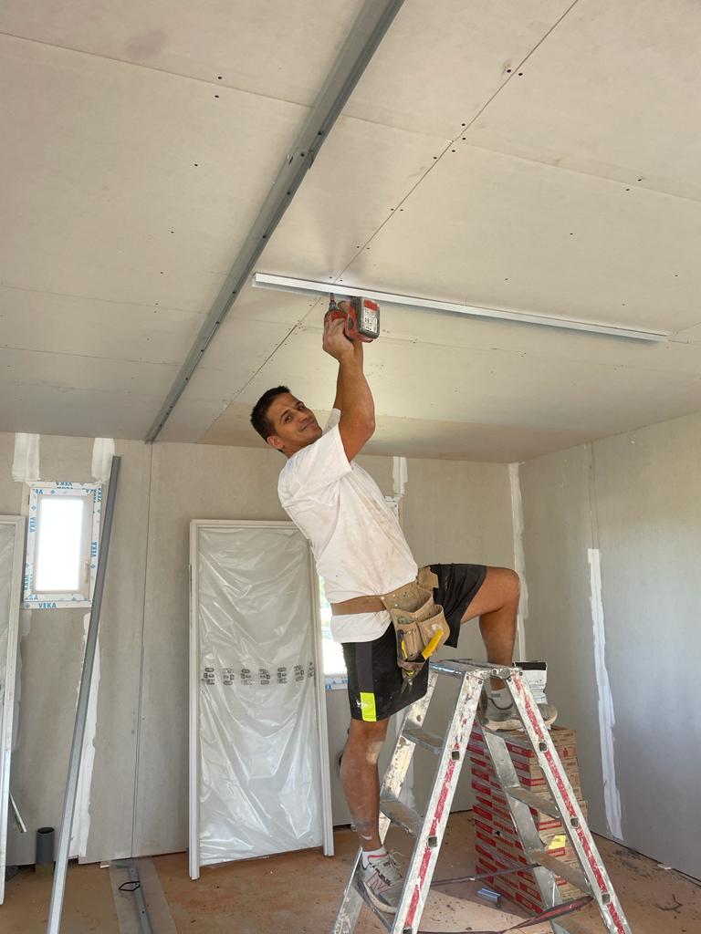 Un homme en train de poser du place au plafond sur une chantier de plâtrerie, agencement et isolation