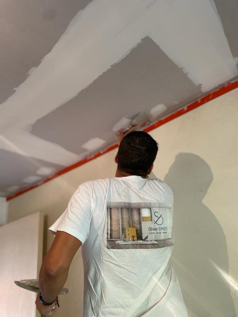 Un homme entrain de poser du placo au plafond sur un chantier